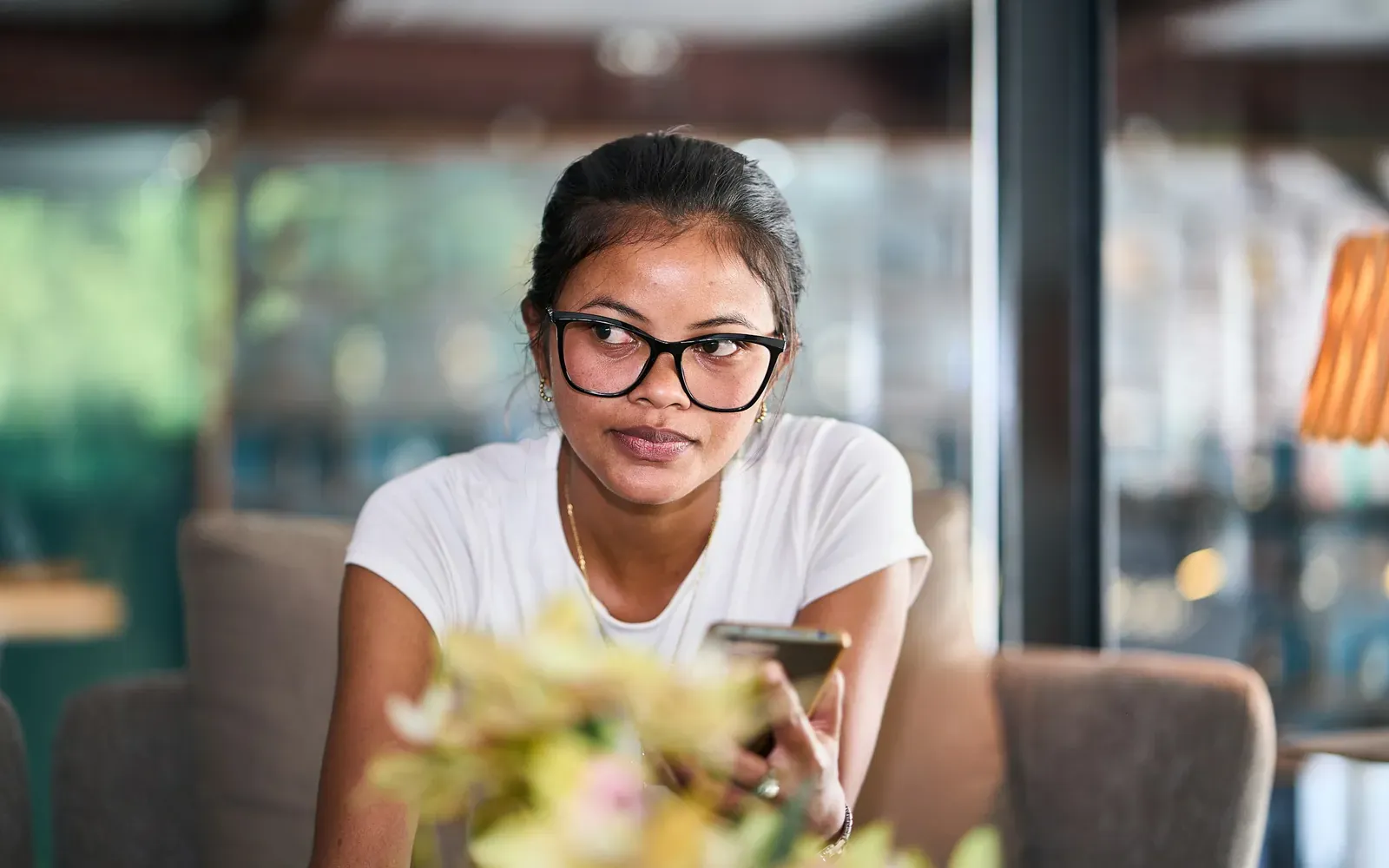 Young professional holding a phone and thinking, representing an H-1B applicant weighing the lottery, the $100K fee and other visa options.