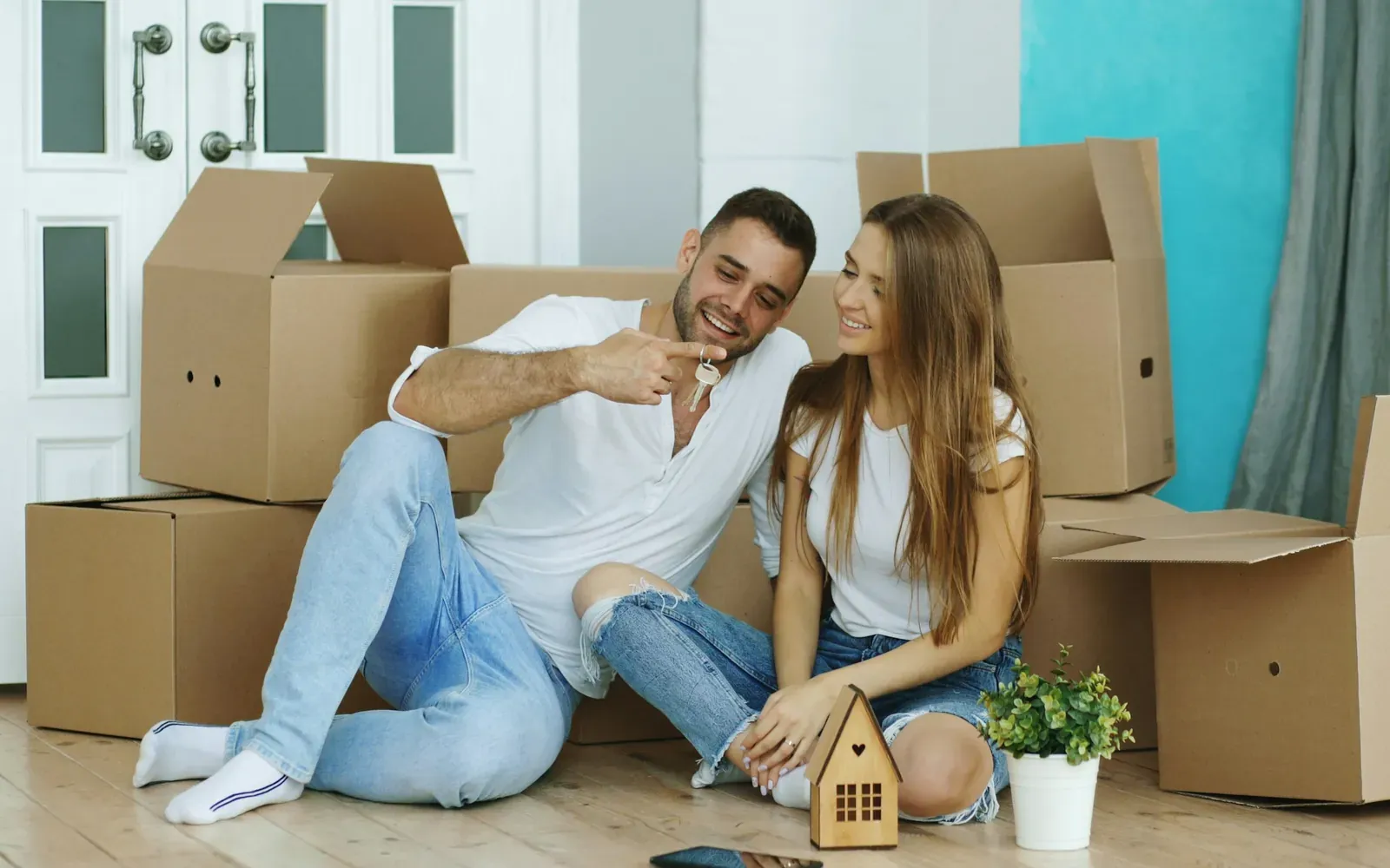 Couple sitting among moving boxes holding new house keys, representing the move from H-1B to a U.S. green card and permanent residence.