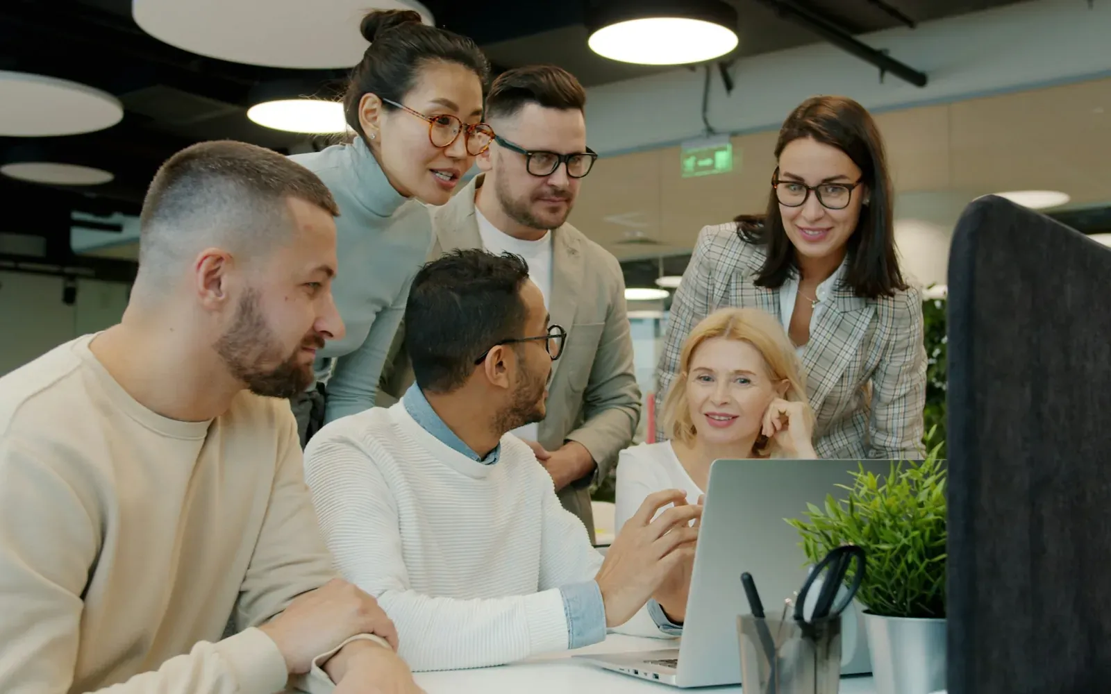 Team of professionals gathered around a laptop in a modern office, representing employers and workers navigating the H-1B visa process.