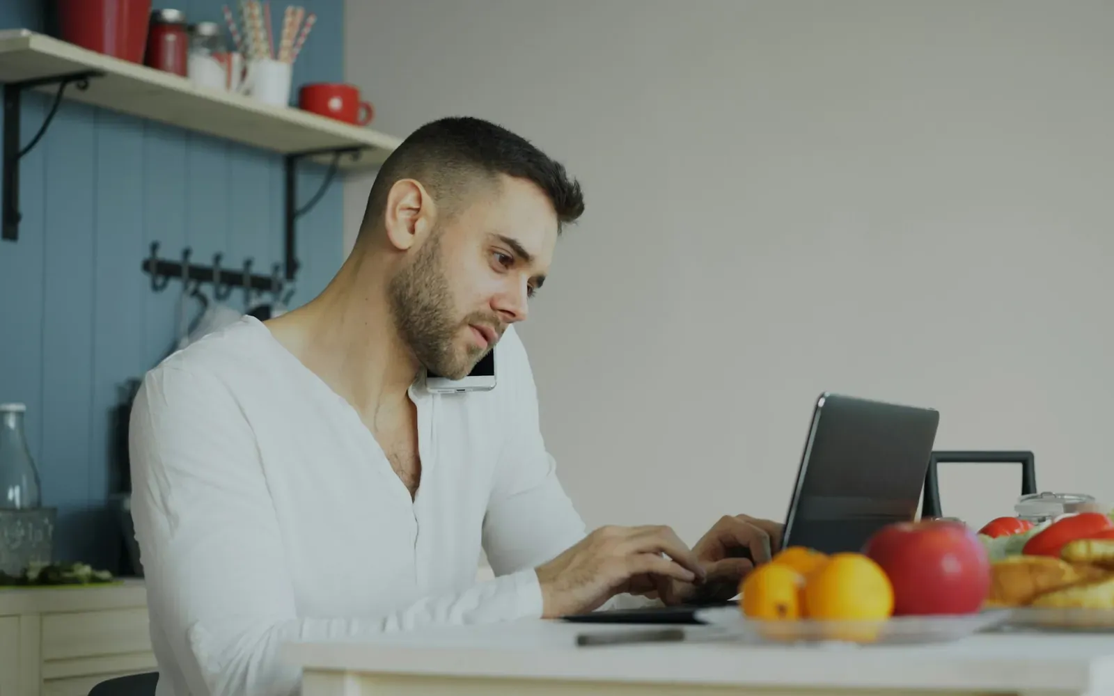 Man working on a laptop at home while on a phone call, representing an H-1B worker using the 60-day grace period to find a new employer after a layoff.