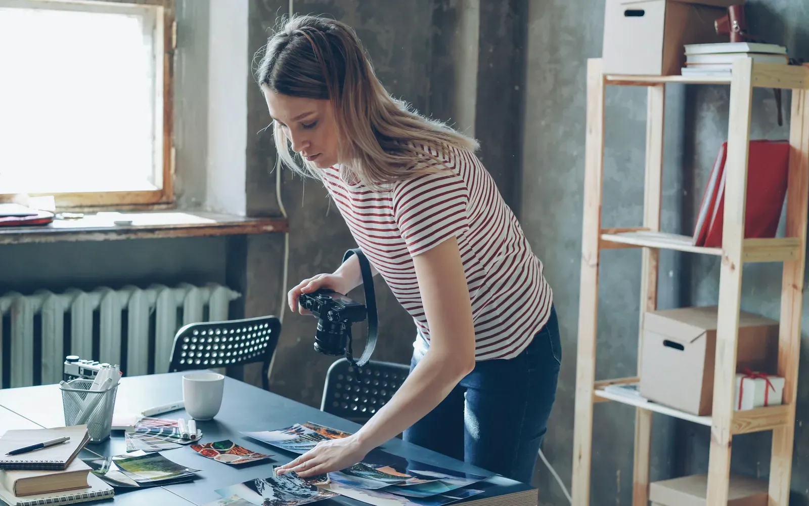 Creative professional with a camera reviewing printed photographs at a studio table, representing building an O-1 visa evidence portfolio.